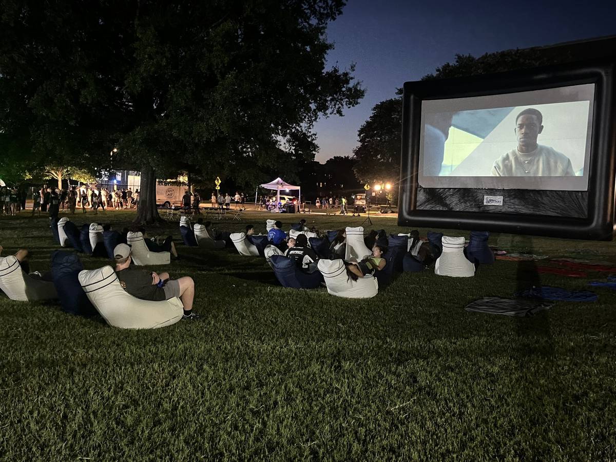 Outdoor movie screen with rows of navy and white bean bag chairs in front of a campus building